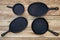 Set of four round and oval cast iron skillets of different sizes on a wooden background. Viewed from above on a rustic wooden deck