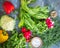 A set of fresh vegetables from a rustic garden of radish, pepper spinach, sliced cabbage, greens, lie on a gray table