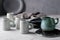 Set of grey rustic coffee cup handcraft and blue ceramic cream jug against shabby grey wall. Natural crockery tableware