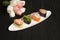 Set of Japanese Gunkans with salmon Sake in cucumber in focus on white plate, black wooden board with pastel tulip flowers