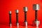 Set of metal silvery dumbbells on a red background with falling shadows. Four dumbbells of different sizes and weights