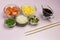 Set of raw vegetables, red fish, rice, soy sauce in glass bowls. Hawaiian dish. Bamboo chopsticks