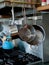 Set of sauce pans hanging to the right of a stove top in a nice kitchen with a stainless steel backsplash and a tea kettle