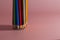 A set of sharpened multi-colored pencils, standing on a pink background on the left side, with a clear shadow from the pencils.