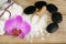 Set for spa treatments with lotions for skin, orchid flowers, bath salt and black stones for a hot massage on a wooden background