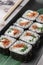 Set of square maki rolls with fried salmon, curd cheese and green bamboo leaf in a black ceramic plate with chopstick on a bright