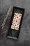 Set of square maki rolls with tiger shrim, caviar and green bamboo leaf in a black ceramic plate with chopstick on a dark gray