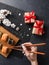 Set of sushi and maki rolls, hand with chopsticks, gift boxes and branch of white flowers on stone table.