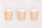 Set of three ribbed coffee kraft paper cups with cap on light wood board, top view.