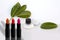 Set of tubes of lipstick stand on a white background with vibrant green leaves, lip gloss in a black jar on a stone, make-up, the