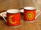 A set of two fine porcelain ware tea coffee cups in red, black and yellow and two saucers on oak wood rustic background.