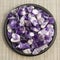 Set of various amethyst natural mineral stones and gemstones on black plate and grey background