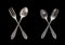 A set of vintage dinnerware: crossed spoons forks and spoons of different shapes and sizes isolated on a black background. Antique