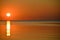 Setting sun on calm mirrored surface of the sea and a boat in distance