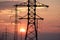 The setting sun in the clouds against the background of the silhouettes of power pylons