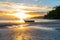 Setting sun glistens on water and sand patterns with dinghy silhouette on beach at low tide