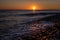 Setting sun on the horizon is reflected in the water and a pebble beach