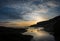 The setting sun and puffball clouds reflected in the lagoon at the beach