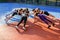 Seven athletic women doing plank on one hands, putting the other hand on each other`s back in the circle on the outdoor