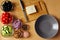 Seven bowls with tomatoes, black olives, cucumbers, colored peppers, pink salt, onion and walnuts. An empty plate and a cutting