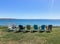 Seven chairs sit on the grass near bluff looking out to sea.