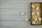 Seven chicken eggs lie in a wooden box on straw and two next to each other on a blue wooden background. The top view