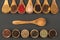 Seven cooking spoons made of olive wood in a row and six small wooden bowls in a row filled with various spices