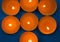 Seven lighted mango-scented candles are shown in close-up. Candles lie on a blue background