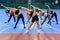 Seven slender sporty young women doing body tilts to left and right sides at the outdoors workout in urban park.