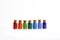 Seven tiny glass bottles with a cork stopper, filled with a rainbow colours of beads, on a white background