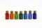 Seven tiny glass bottles with a cork stopper, filled with a rainbow colours of beads, on a white background