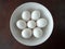 Seven White Eggs in a White Bowl against a Brown Background