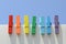 Seven wooden multi-colored clothespins, painted in the colors of the rainbow, against the blue sky