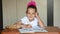 Seven-year girl schoolgirl doing homework distracted and looked into frame