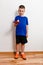 Seven-year-old boy in a blue T-shirt kicks a ball on a table tennis racket against a white background