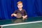 Seven years boy holding a black racket for table tennis indoors