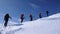 Several backcountry skiers hike and climb to a remote mountain peak in Switzerland on a beautiful winter day