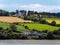 Several buildings and trees on a hill. Irish summer landscape. Picturesque countryside. Farm fields under a blue sky, house on