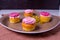 Several colorfully decorated cupcakes on a plate with daisies