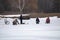 Several fishermen sit on boxes on the thin spring ice far from the shore and fishing.