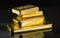 Several gold bars of different weight on a dark mirror surface