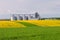 Several granaries with a field of blooming canola and wheat in t