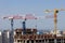 Several high-rise cranes at a construction site, together with people, are building a modern apartment building.