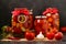 Several jars tomatoes are located on a table, on a dark background