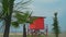 Several palm trees on the background of a red lifeguard tower on the coastline. Bright shots, concept of vacation on the