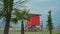 Several palm trees on the background of a red lifeguard tower on the coastline. Bright shots, concept of vacation on the