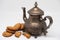 Several pieces of oatmeal cookies lie by a vintage copper Arabic teapot