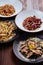 Several plates of pasta with different kinds of sauce over wooden background, top view.