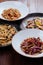 Several plates of pasta with different kinds of sauce over wooden background, top view.