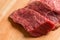 Several portioned pieces of meat for steaks lie on a wooden cutting board.
